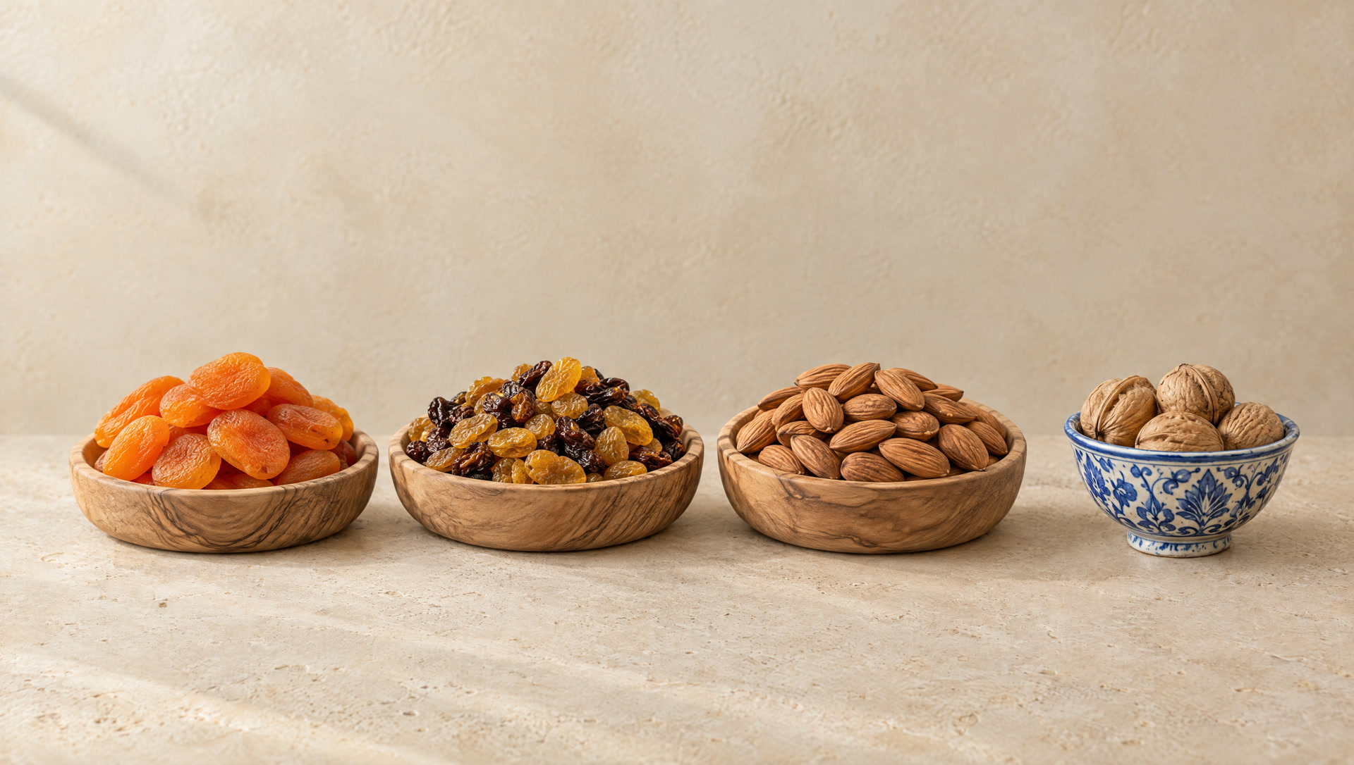 Dried apricots, raisins and almonds in wooden bowls beside a blue Rishtan dish of walnuts